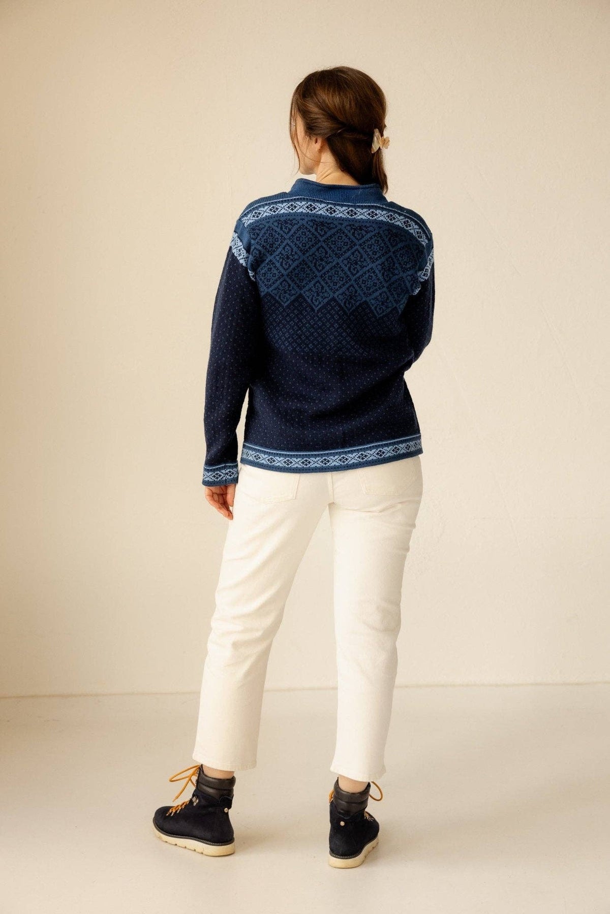 A person wearing a Norwegian wool cardigan with a geometric yoke pattern, white jeans, and dark boots.