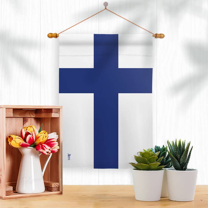 The Flag: Finland Garden Flag - Finnish Nationality Home Decor Flag hangs on a white wall above a table with a crate of flowers and two succulents, adding Finnish decor to your space.