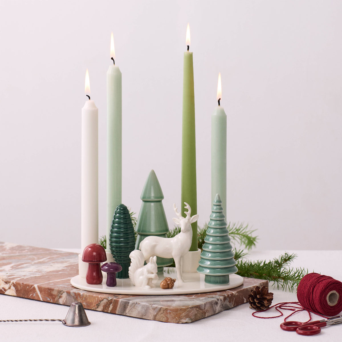 Nordic advent candle holder with four lit taper candles on a marble base, decorated with miniature ceramic deer, a squirrel, trees, and mushrooms.