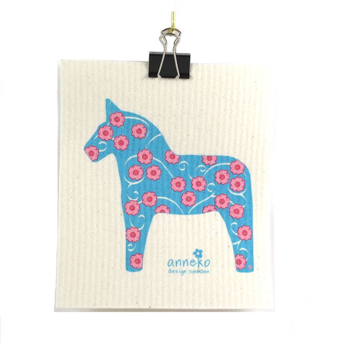 The eco-friendly Dish Cloth: Dalahäst Turquoise Dala Horse by Anneko Design Sweden features a turquoise Dala horse and pink flowers, clipped at the top with a black binder clip and "anneko design sweden" printed below the illustration.