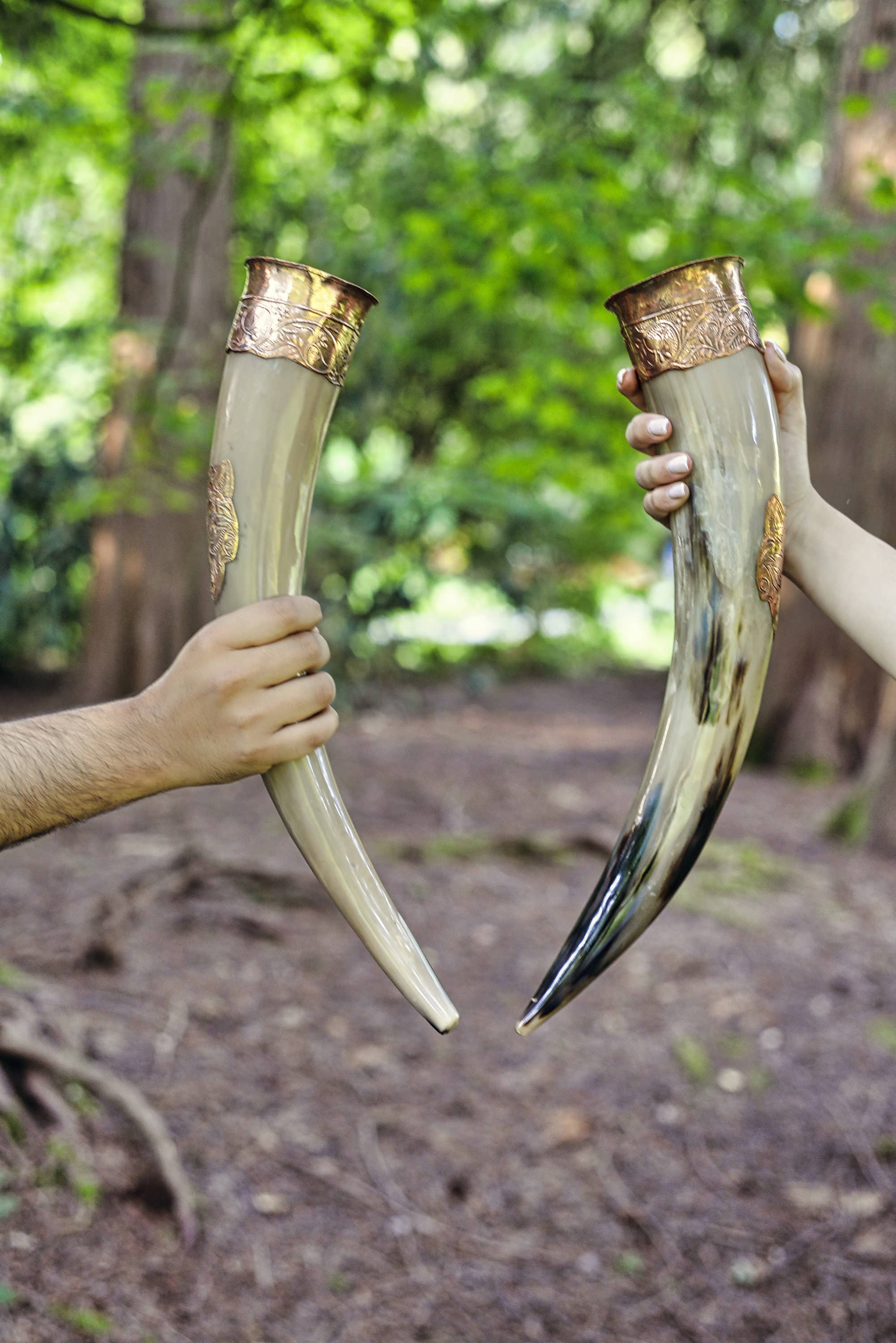 Two people outdoors clink Drinking Horn: Authentic Viking Wedding Gift—genuine ox horn with gold detailing—creating the perfect unique moment for couples.