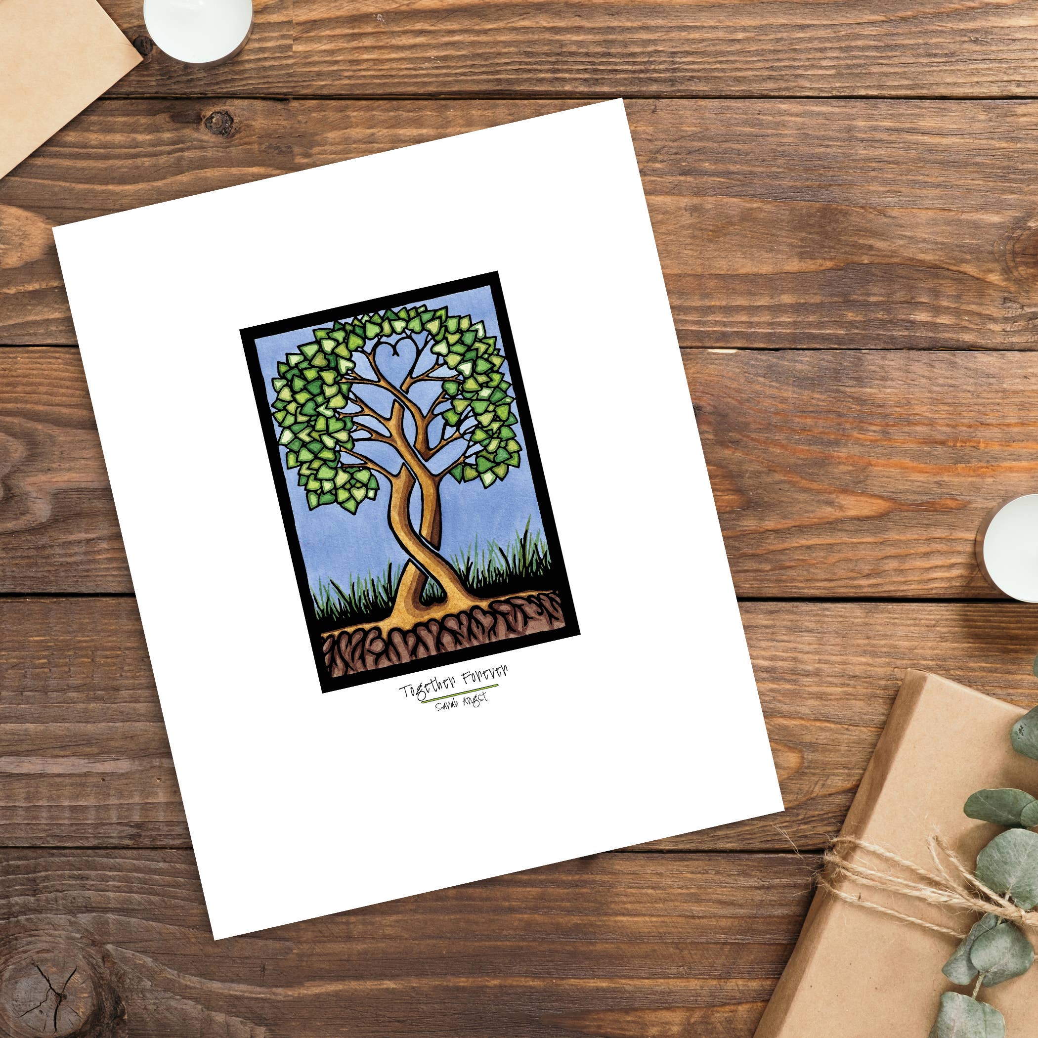 The "Together Forever Tree" giclee print by Sarah Angst features heart-shaped leaves and comes in 8"x10" or 11"x14" sizes on white paper, displayed on wood with a candle, gift, and envelope nearby.