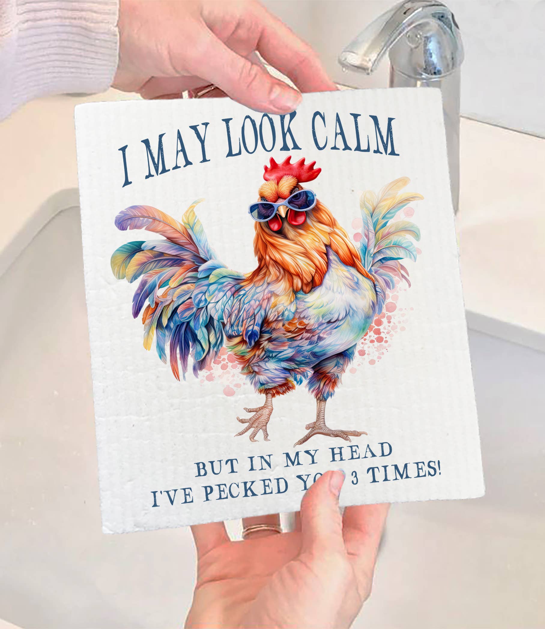 A person holds the eco-friendly Dish Cloth: May Look Calm Funny Saying SWEDISH DISH CLOTH, featuring a colorful rooster in sunglasses and the phrase, “I may look calm but in my head I’ve pecked you 3 times!”—a quirky kitchen addition.