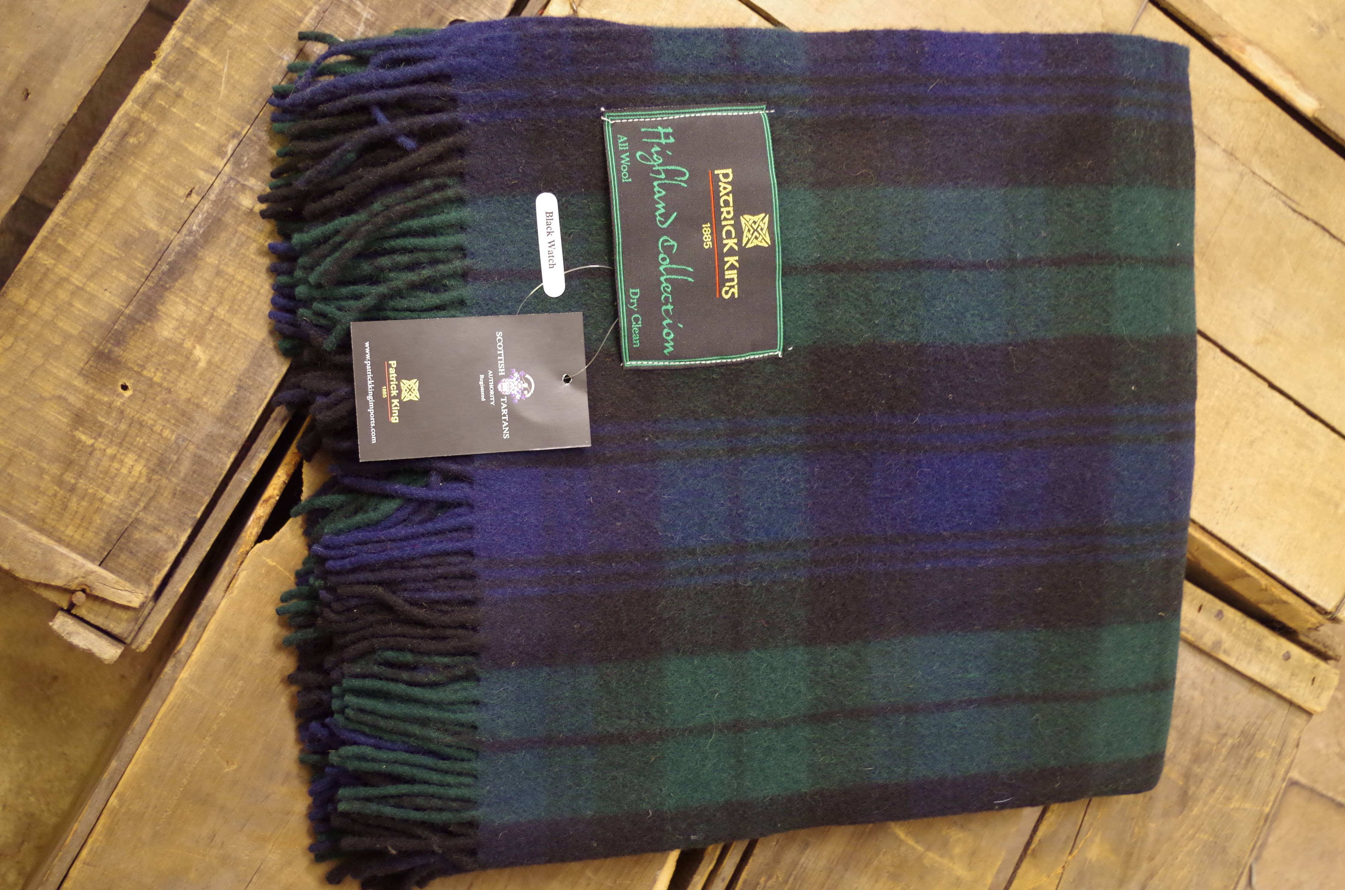 A folded Blanket: Black Watch Highland Blanket with green, navy, and black checks from the Patrick King Highland Collection rests on a wooden surface.