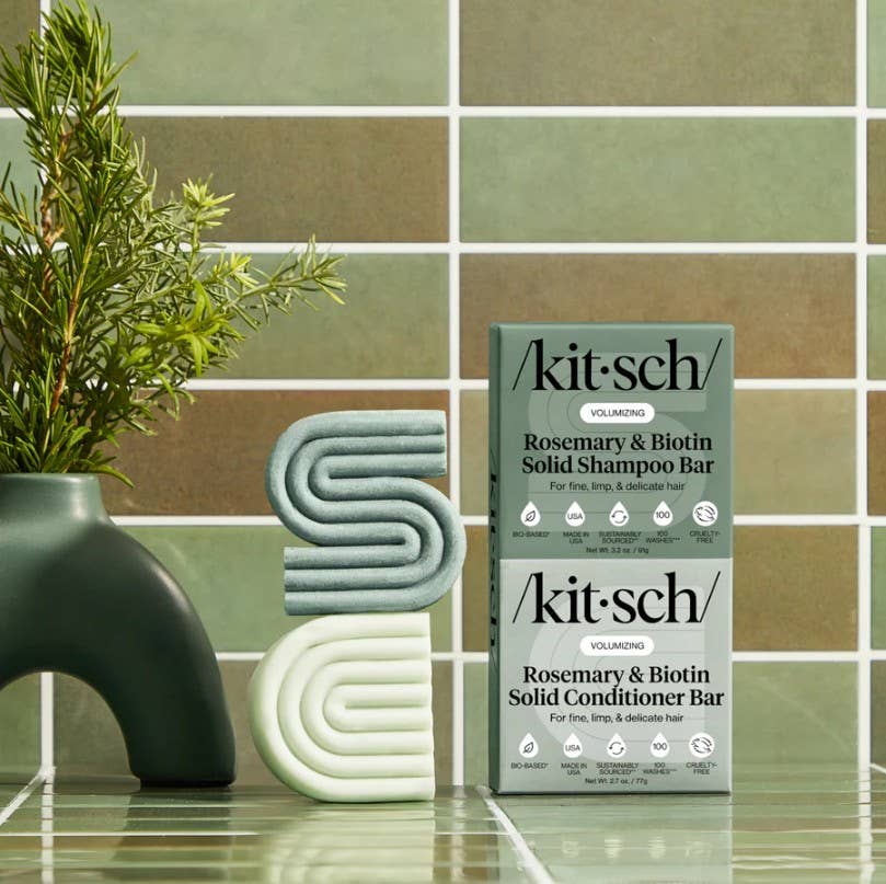 Two boxes of Kitsch Hair: Rosemary & Biotin Volumizing Shampoo & Conditioner Bar Combo (2 bars, 2.7oz each) are displayed with modern soap bars and a rosemary vase on tile—ideal haircare for fine hair.