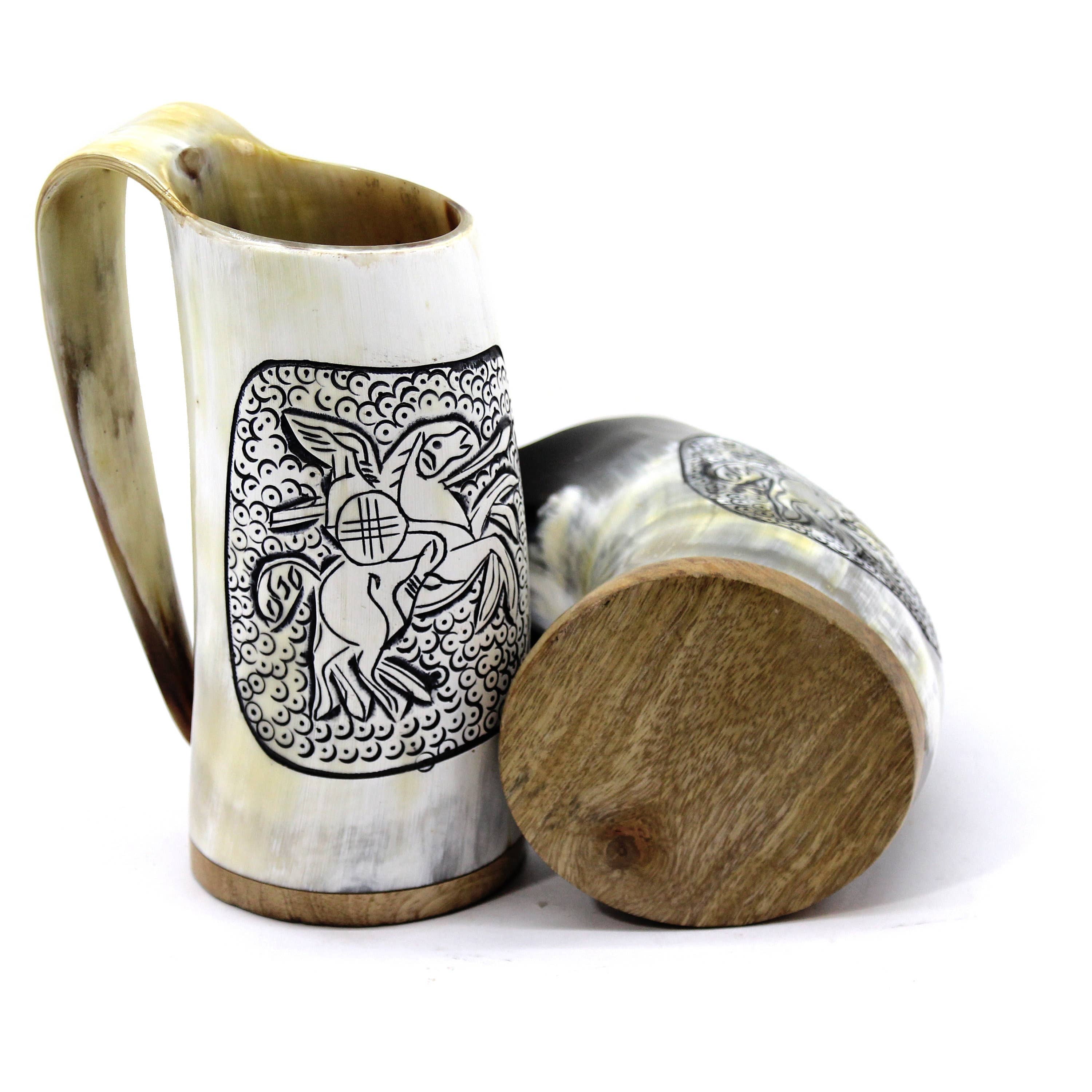 A pair of hand-crafted Horn Mugs, each with a wooden base, includes one upright and one lying flat. They are adorned with intricate black designs depicting a mythical creature, echoing the aesthetic of Viking Drinking Horn Mugs.