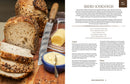 Sliced multigrain bread on a cutting board with a knife and butter; the book Bring Home the Bakery Sourdough Recipes for High Hydration Breads, Laminated Pastries and Swedish Buns by Grego Montalban Sanchez & Hanna Lofgren is shown on the right.