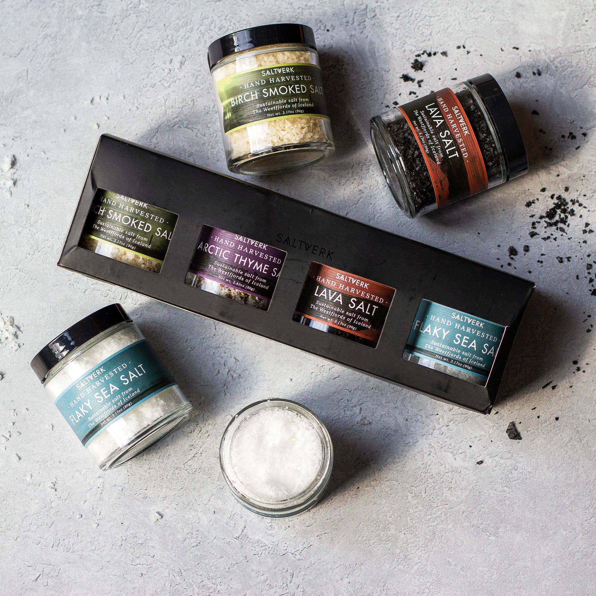 The SALTVERK Gift Set, featuring flaky sea salt, lava salt, birch smoked salt, and arctic thyme salt jars, is displayed on a light gray surface.