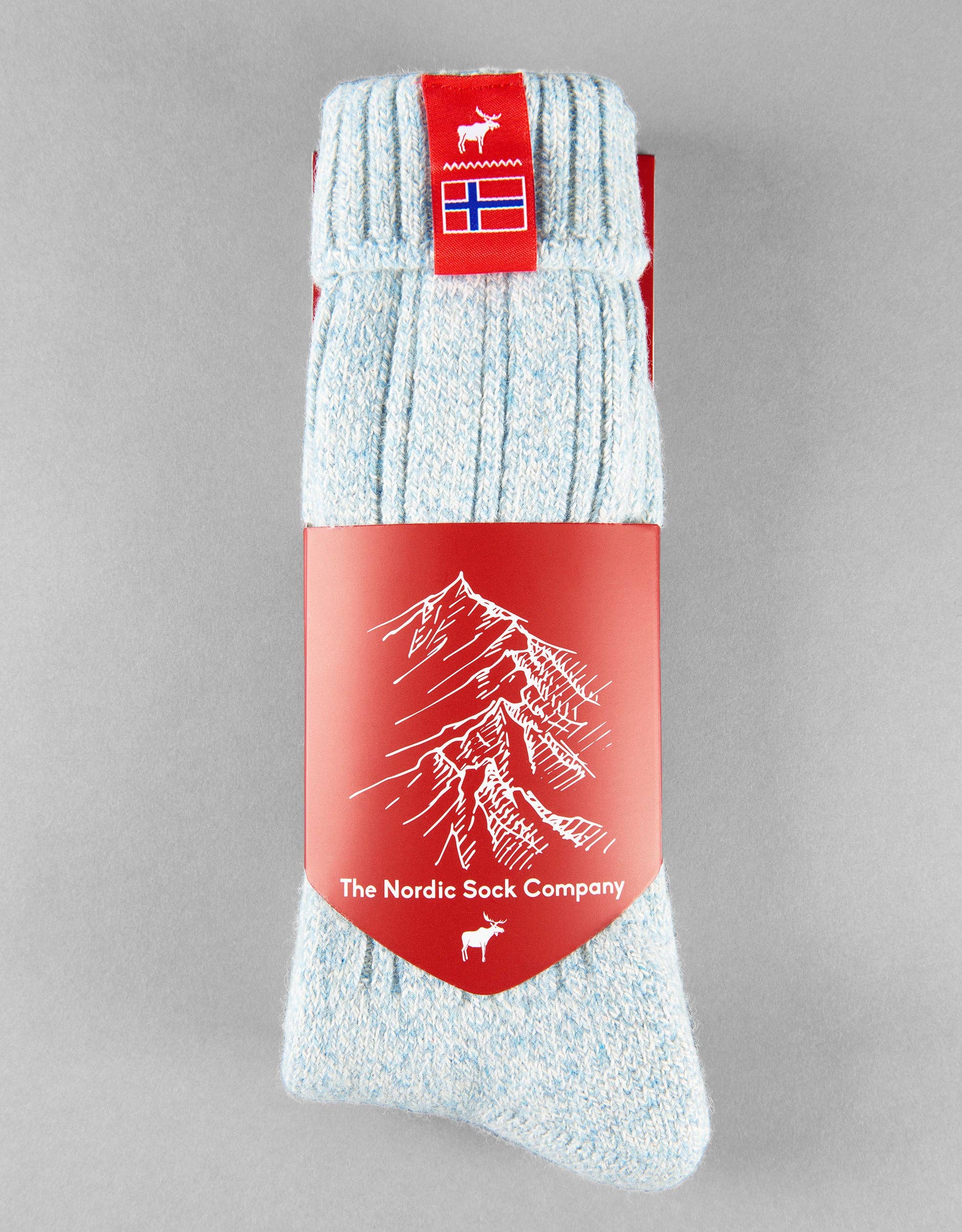 Light blue Norwegian Fjord Socks from The Nordic Sock Company, packaged with a red label featuring a mountain illustration and small Norwegian flag—ideal wellie socks for outdoor adventures.