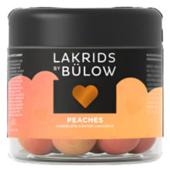 A clear jar with a black lid labeled Lakrids By Bülow - Peaches contains 125g of Danish chocolate-coated licorice balls in peach hues—a delicious Scandinavian treat.