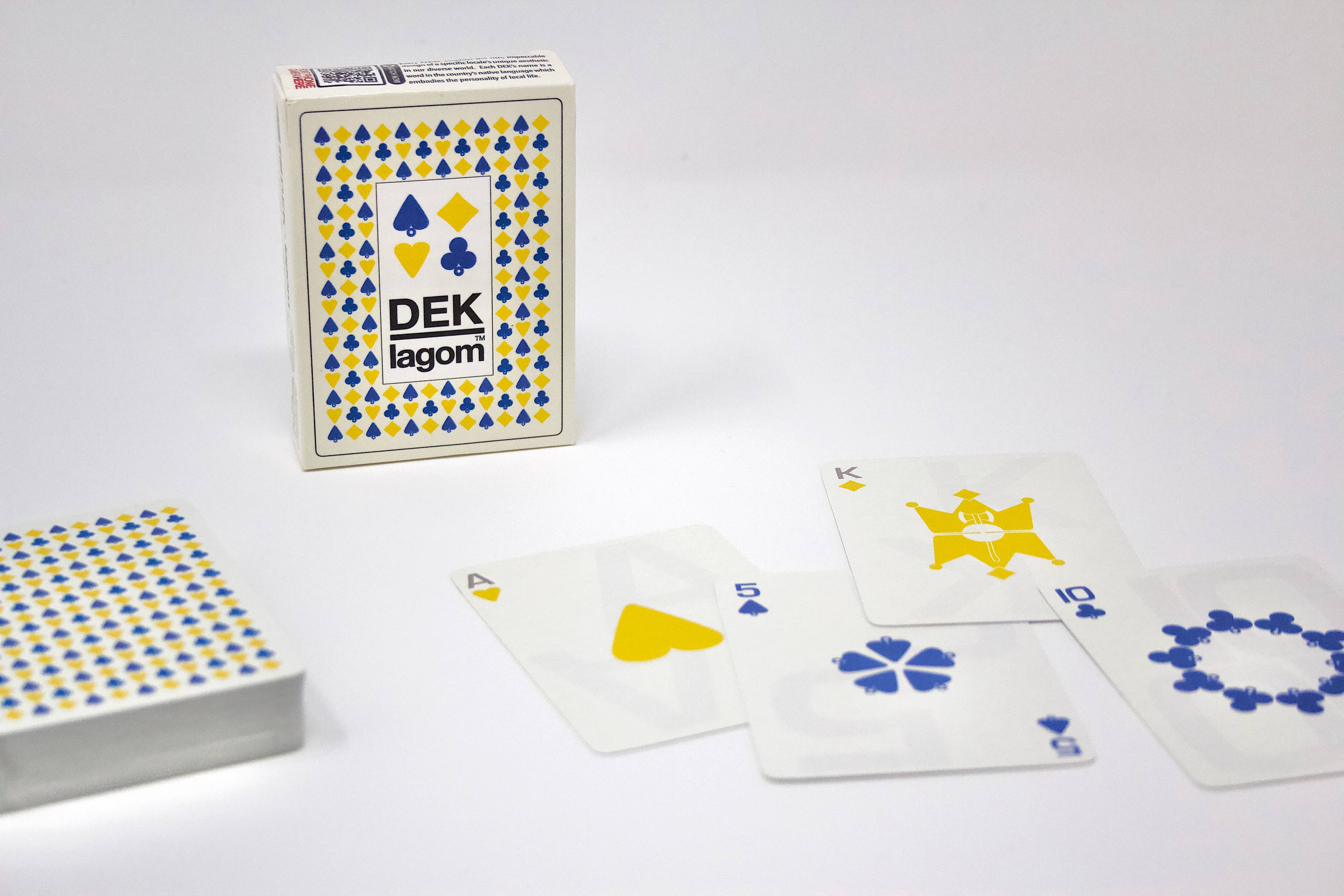 A deck of Playing Cards: DEK Lagom (Sweden), presented in a box labeled with the product name. The cards, laid out on the table, feature custom symbols in blue and yellow, capturing the essence of Scandinavian elegance and balanced living.
