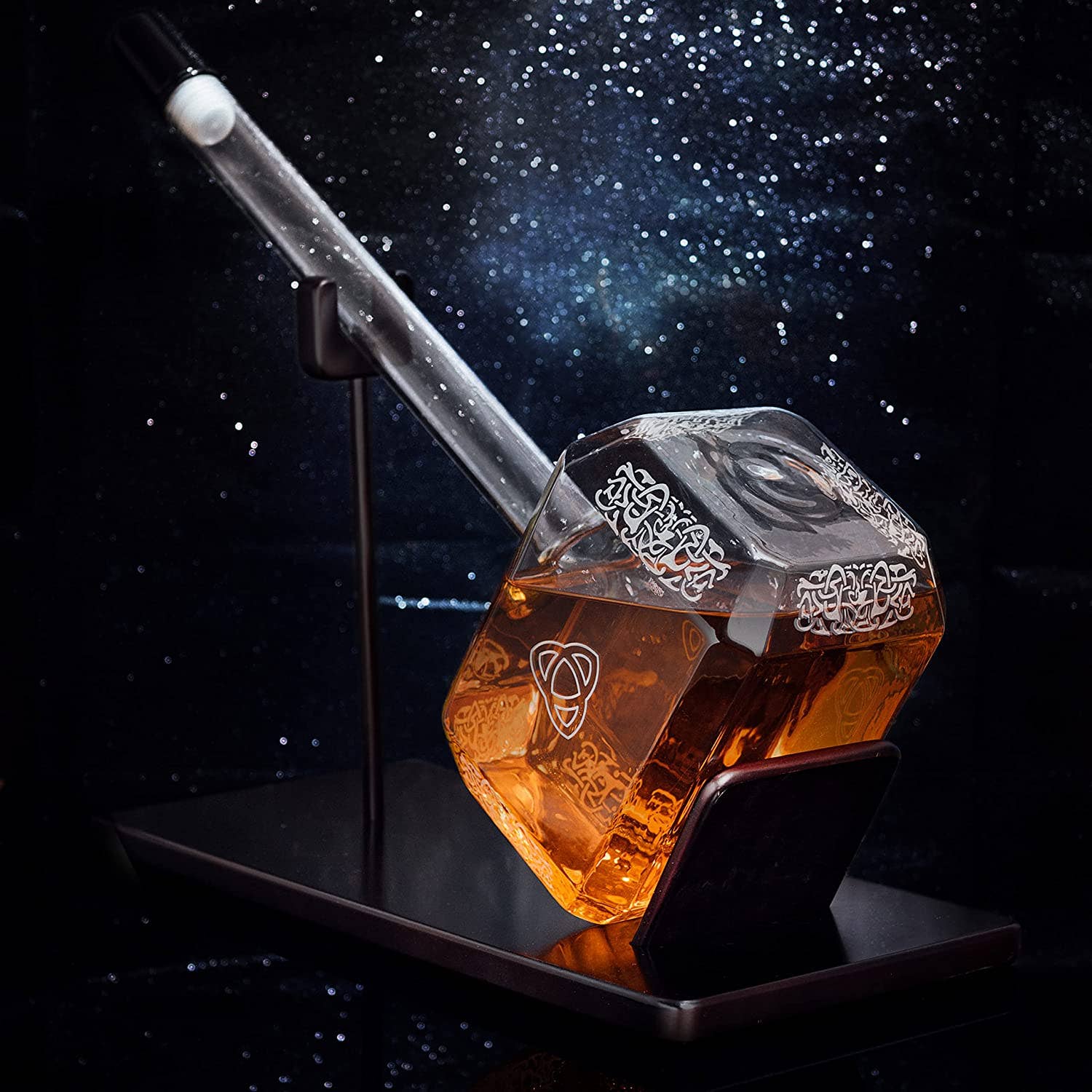The Decanter: Thor Hammer Whiskey and Wine Decanter 3500ml, shaped like Mjolnir and shown with amber liquid on a black stand against a starry background, is the ideal Norse mythology barware for Viking whiskey fans.