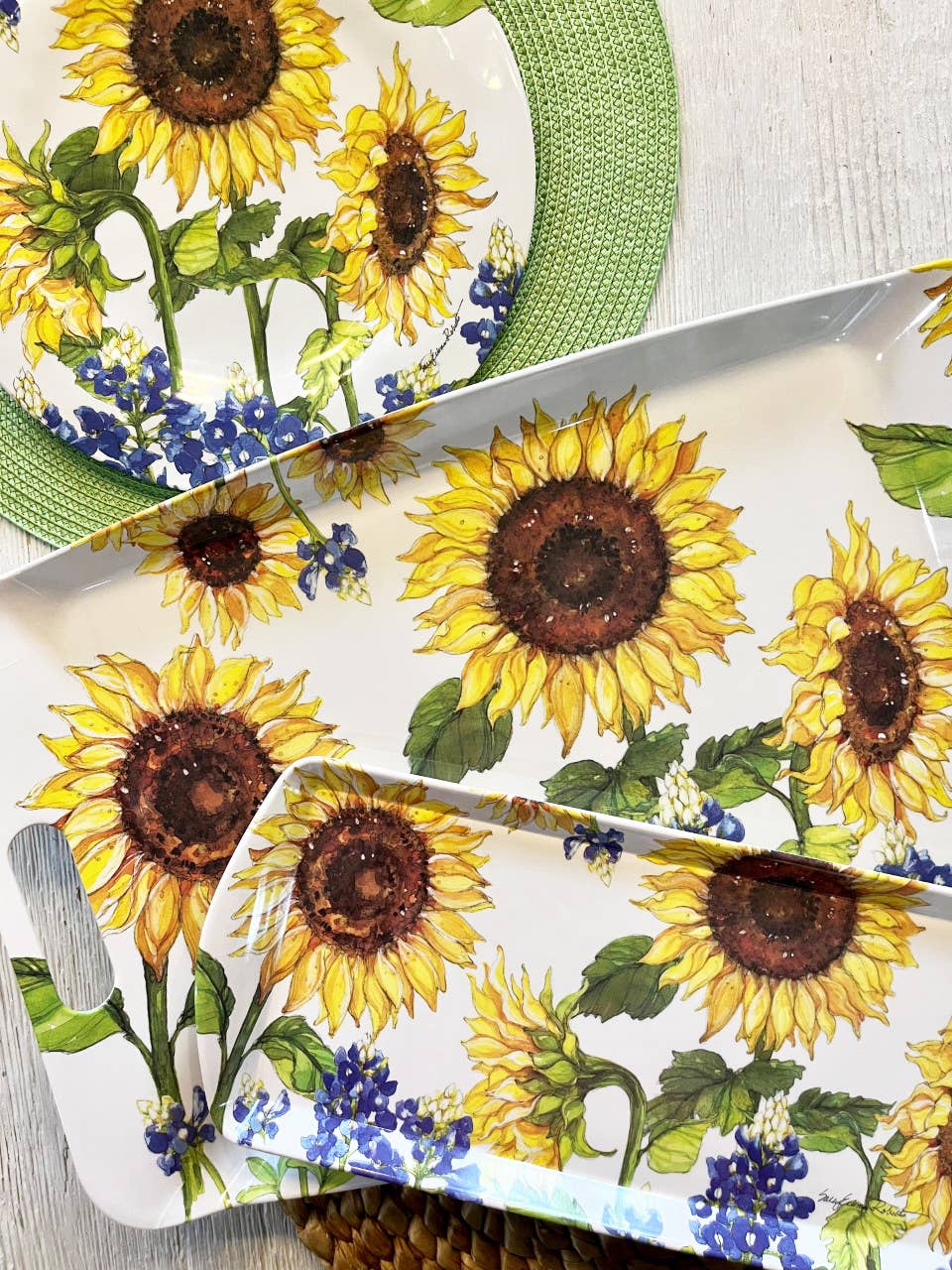 The eco-friendly Sunflower & Bluebonnets Floral Loaf Serving Charcuterie Tray features large sunflower and blue flower designs, displayed on a light surface with green and woven placemats.