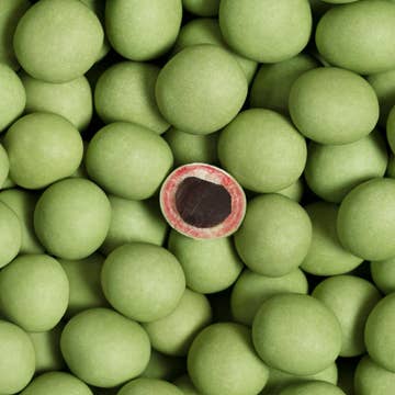 A group of green peas with one cut open in the center resembles the limited-edition Lakrids: Sour Strawberry Danish Gourmet Licorice by Bulow, 4.41 oz, revealing its rich interior.