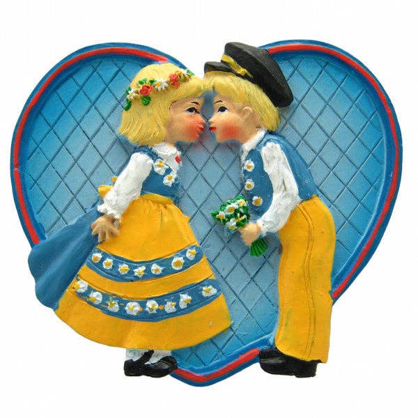 The Magnet: Swedish Kissing Couple Party Favor Kitchen Magnet features two cartoon children dressed in traditional Swedish attire, standing before a blue heart backdrop. The children face each other as if about to share a kiss, while the girl holds flowers behind her back. This delightful scene makes for an adorable novelty gift ideal for any occasion in your kitchen.