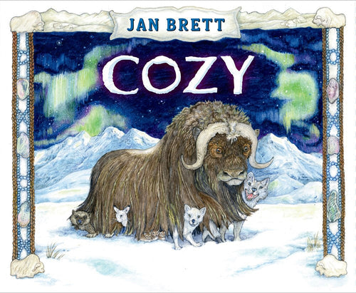 A musk ox stands in snowy mountains beneath the northern lights, with four small white foxes beside it—an enchanting scene from "Book: Cozy by Jan Brett," an Alaska winter tale of animal friendship. "Jan Brett" and "Cozy" are written above.
