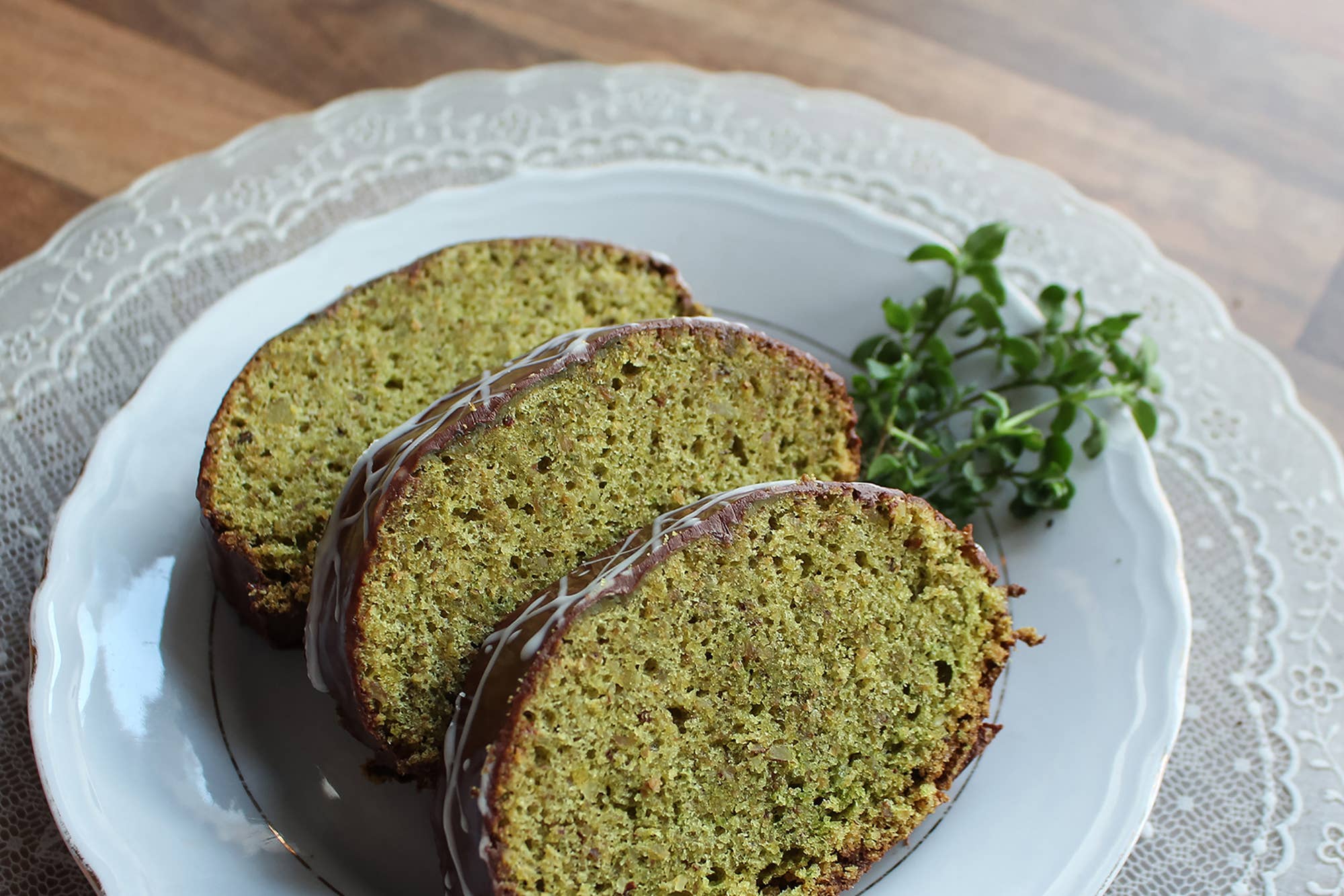 Three slices of green almond cake with glaze sit on a white plate, garnished with fresh herbs—perfectly baked in the Rehrucken / Almond Cake Loaf Pan for easy release thanks to its non-stick surface.