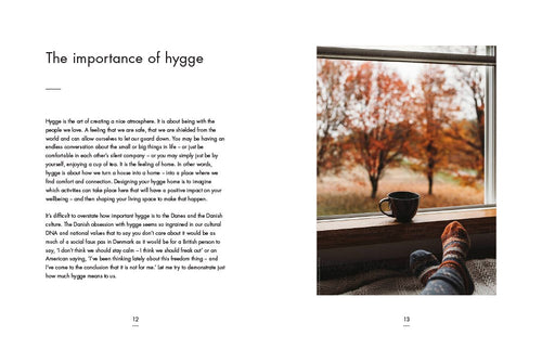 An open copy of "Book: My Hygge Home" reveals text on the left and a photograph on the right, depicting a Hygge-inspired autumn scene. The image shows someone wearing socks with their feet propped up by a window, accompanied by a mug, all set against a backdrop of tree views. This cozy setting perfectly encapsulates the essence of Danish design in creating spaces that evoke feelings of happiness and home.