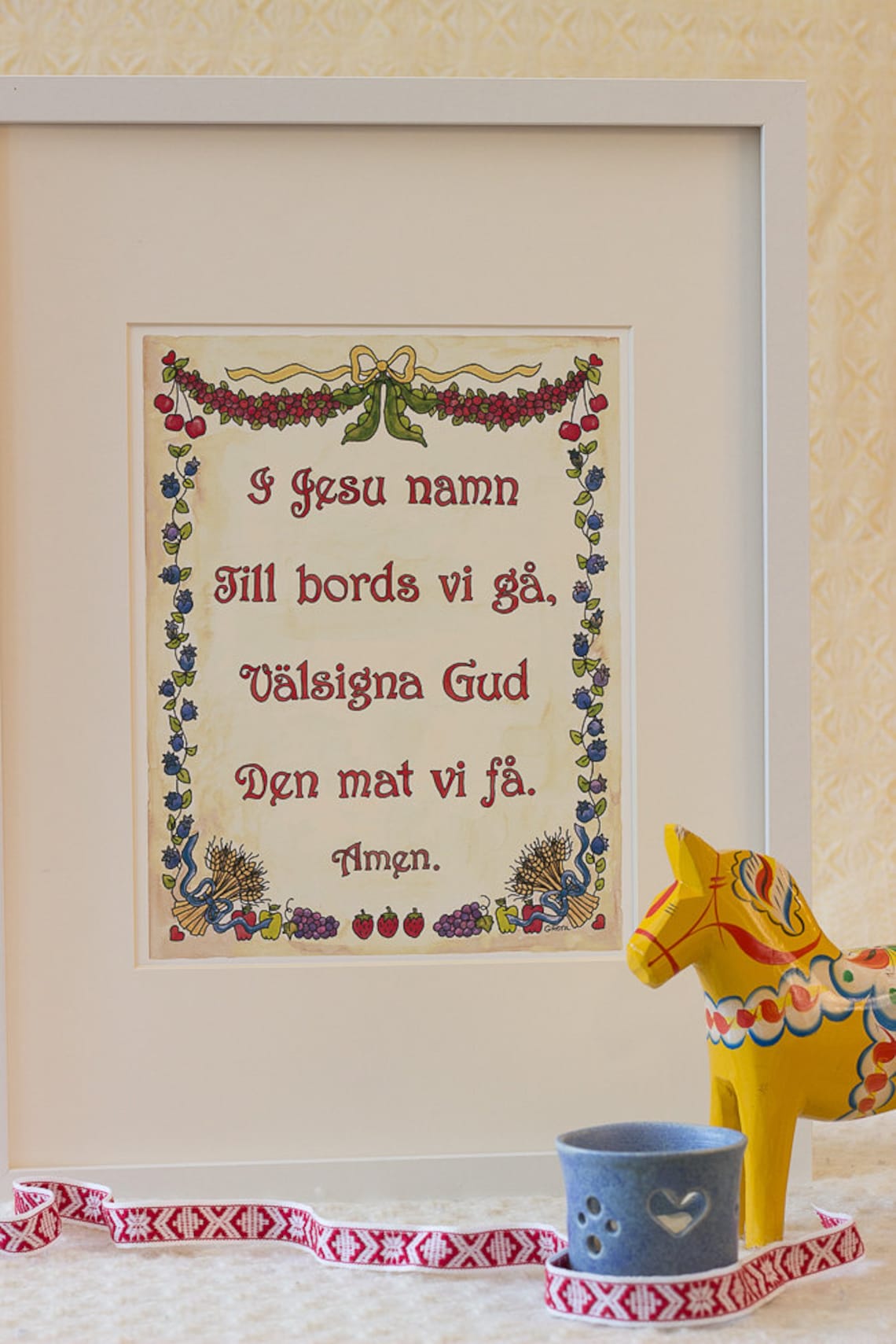 Artwork: "I Jesu Namn" In Jesus Name Prayer by Swedish artist Greta Lann (8x10), displayed in a decorative frame beside a painted Dala horse and blue cup on a patterned surface. Features the Swedish prayer phrase.