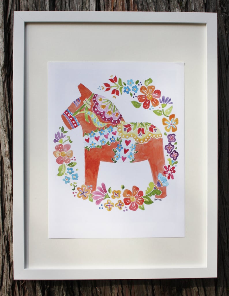 Framed artwork Dala Horse by Greta Lann features a colorful Dala Horse with floral patterns, encircled by a vibrant floral wreath, reflecting traditional Swedish symbols.