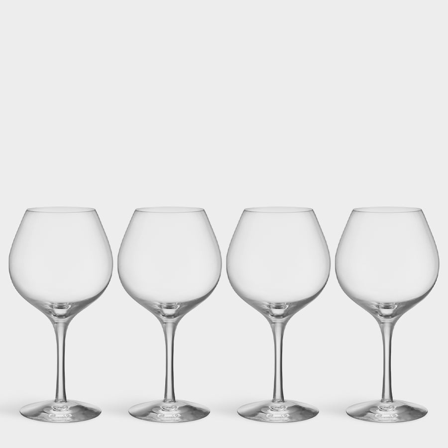 Four Orrefors-inspired More Pinot Glasses arranged in a row, their long crystal stems against a white background, exude elegance and sophistication.