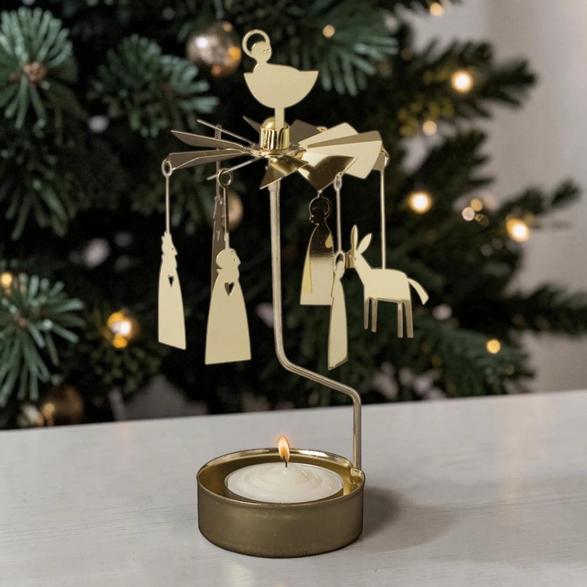 Gold-tone metal Swedish angel chimes with hanging donkey and angel figures and a lit tea light candle at the base.