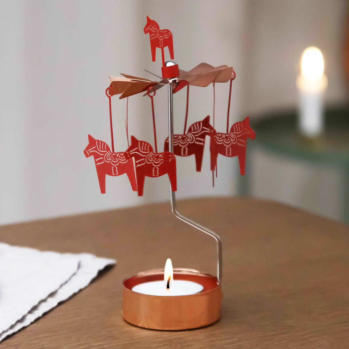 Rose gold Dala horse rotary candle holder with a lit tealight on a wooden table, Scandinavian decor visible in the softly lit background.