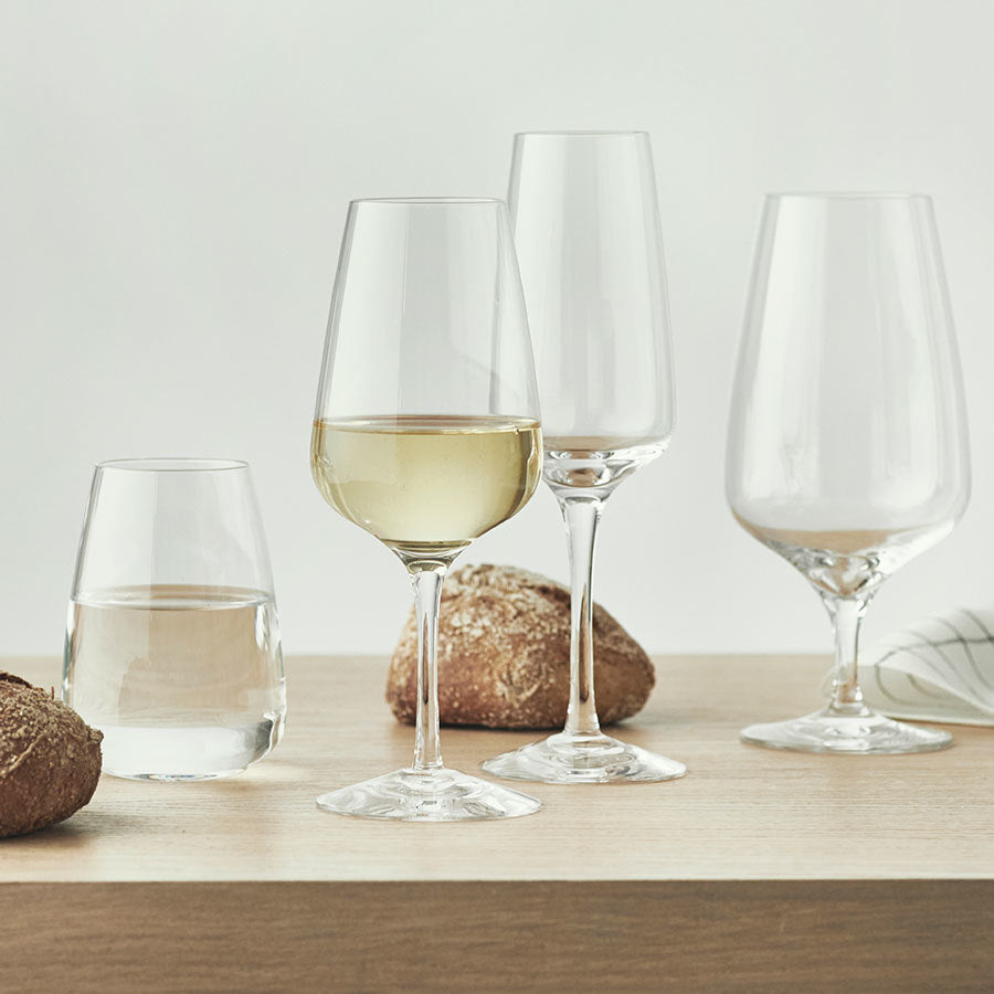 On a wooden table with bread are four glasses, including two wine glasses and a sleek Champagne glass from the Orrefors: Pulse Champagne Glass (4-Pack).