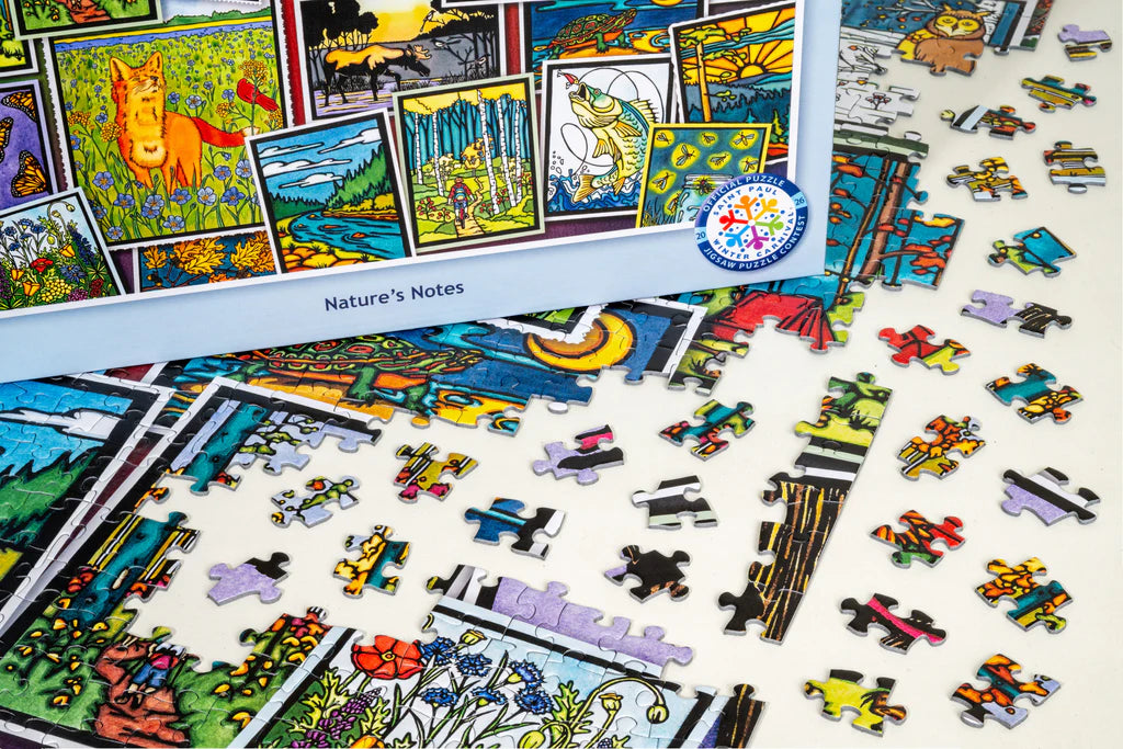 Vibrant jigsaw puzzle pieces are spread across a table, with several connected to form part of the picture. The Maynards box features Sarah Angst’s nature-themed artwork of animals, flowers, and landscapes. The title “Puzzle: Nature’s Notes 1000 Piece ‘Mixed Up!’ PuzzleTwist Jigsaw Puzzle” is clearly shown—a delightful activity for a peaceful afternoon.