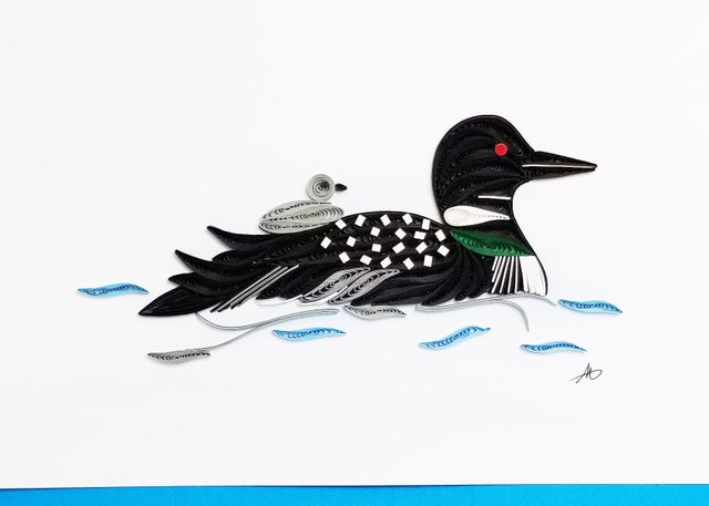 The Cards: Loon Quilling Card 5x7 features Minnesota’s state bird with a chick on its back, gliding across blue water; blank inside for personalization and comes with an aqua envelope in a plastic sleeve—ideal for nature lovers.