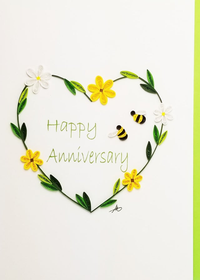 A handmade quilled card featuring a flower heart and bumble bees frames “Happy Anniversary,” making it a charming way to celebrate love on a special day.