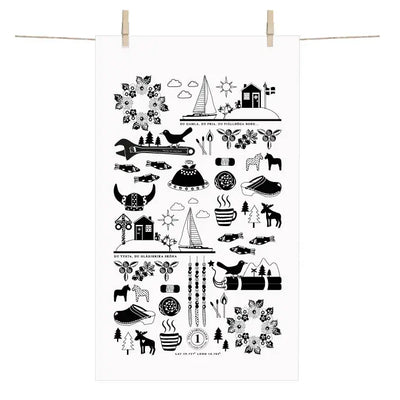 The Made in Sweden Terry-Cotton Towel by Anneko Design Sweden, featuring black Scandinavian-style illustrations on white cotton, including birds, trees, houses, and the iconic Dala horse, hangs on a clothesline with wooden clothespins.
