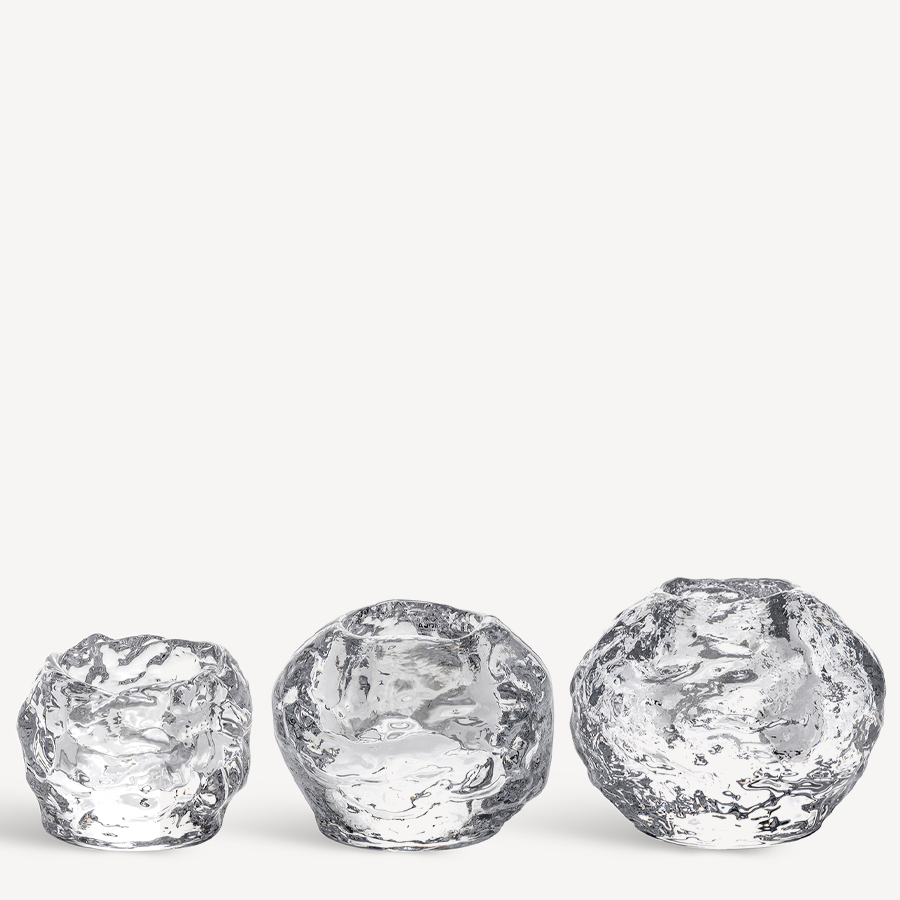 The KostaBoda: Snowball Votive Set of 3, designed by Ann Wolff, features clear glass candle holders with organic shapes, displayed in a row against a white background.