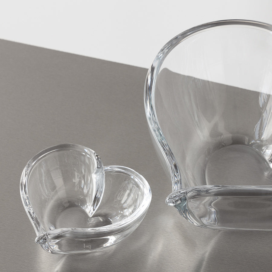 Two clear glass bowls rest elegantly on a metallic surface. The smaller, an Orrefors: Heart Bowl/Votive Small, complements the larger round bowl with its open top. Perfect for adding charm or serving as a votive centerpiece.