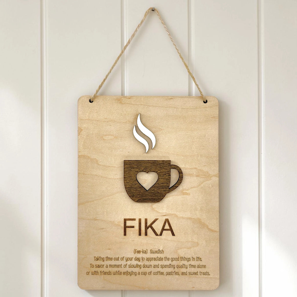 A Scandinavian-style wall sign on a white wall featuring a coffee cup graphic and the word FIKA in bold letters.