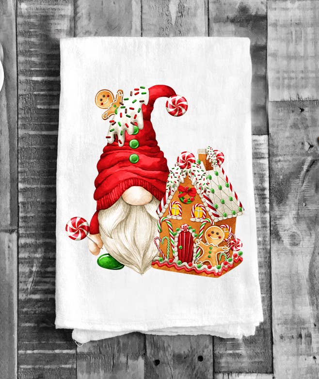The Tea Towel: Christmas Gnome Gingerbread House Flour Sack Tea Towel features a festive white cotton design with a gnome in a red hat holding candy beside a decorated gingerbread house and gingerbread figures.