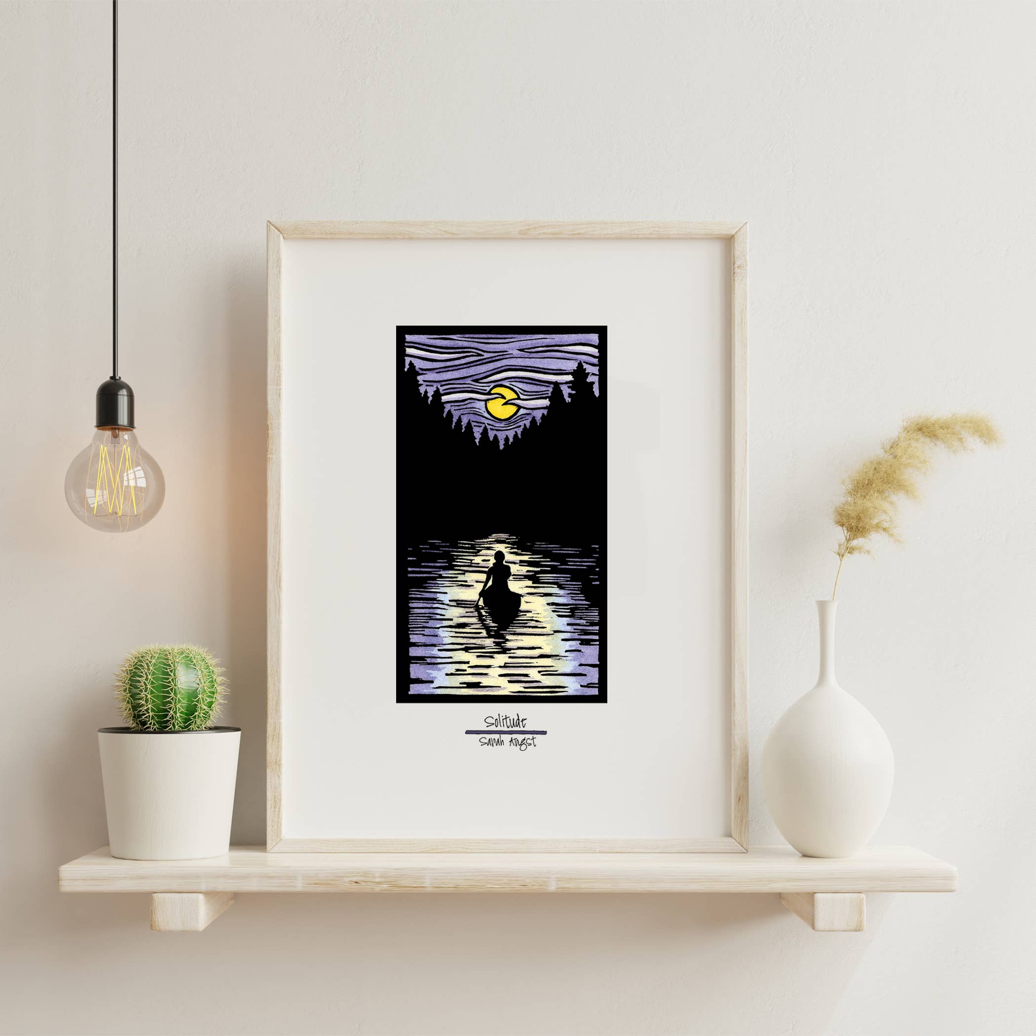 On a shelf sits the "Solitude Canoe" 11"x14" giclee print, expertly framed and capturing a silhouetted figure peacefully canoeing across a moonlit lake under a purple sky. This Sarah Angst artwork is complemented by the presence of a cactus, vase, and hanging bulb, emanating an aura of serene tranquility.