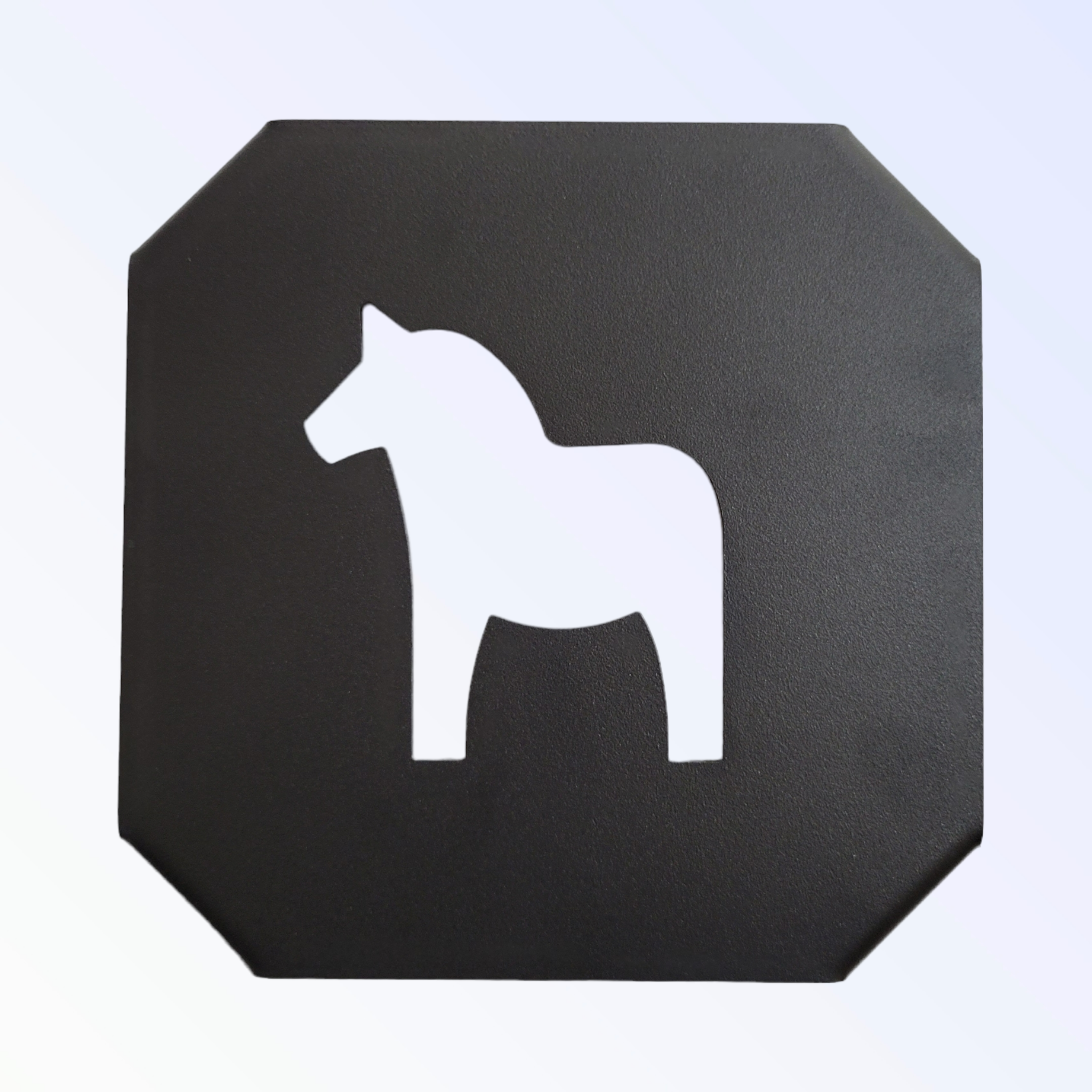 A black cast iron trivet features a white silhouette of a Swedish Dala Horse.