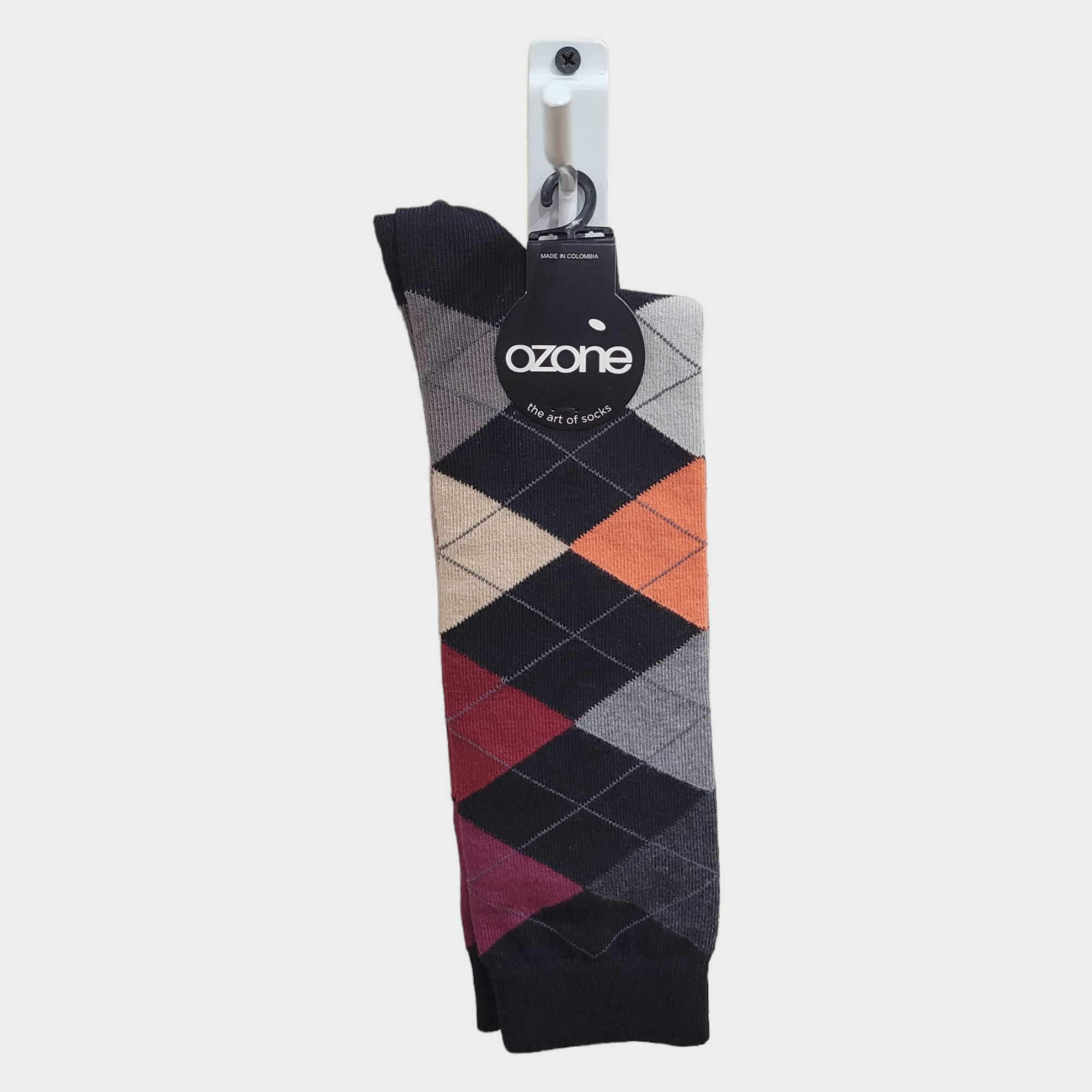 A vibrant multicolored argyle sock hangs on a hook sporting Ozones distinctive black tag. This Classic Argyle design is perfect for those seeking stylish socks with a touch of Ozone Design flair. Product Name: Socks: Ozone - Mens Carnival - Classic Argyle Pattern.