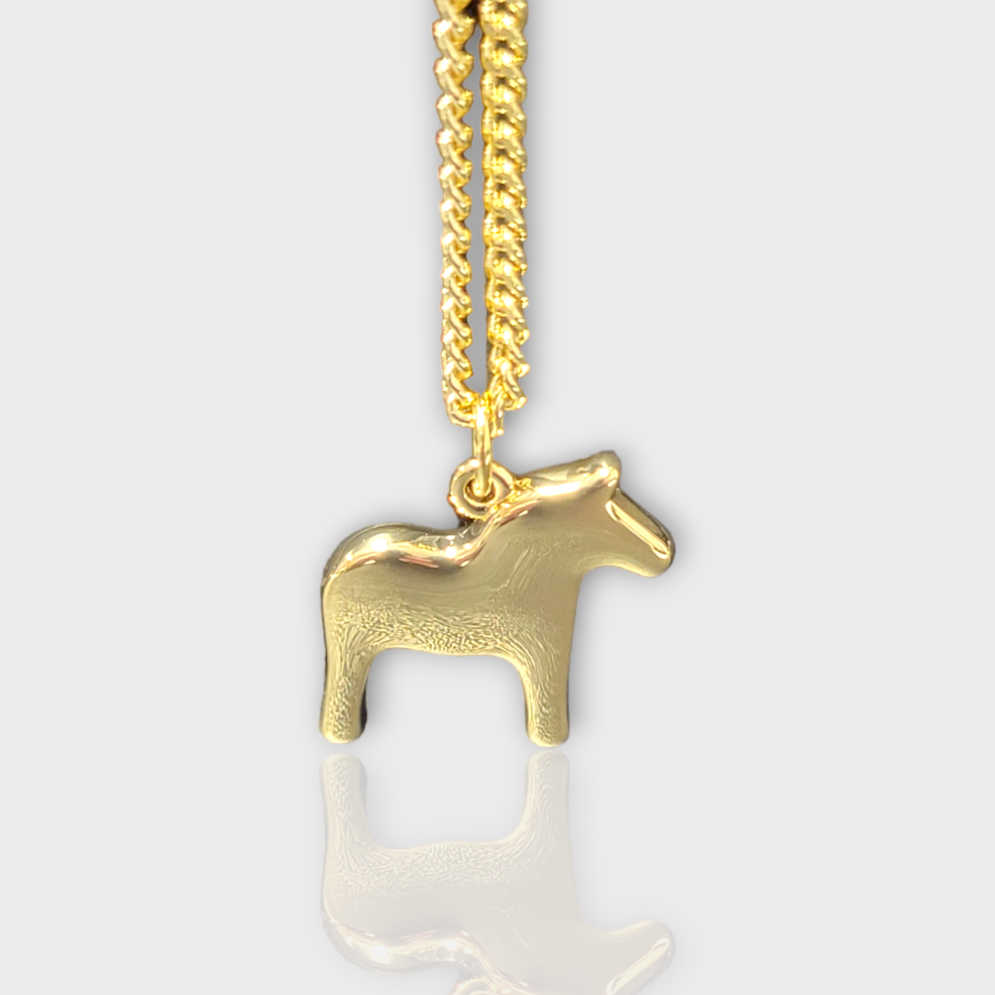 The Dala Horse Necklace by Anna Viktoria, featuring a gold horse-shaped pendant on a fine chain, embodies the elegance of Scandinavian jewelry and highlights the traditional Swedish symbol against a plain background.