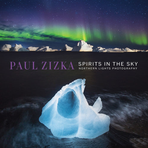 A glowing iceberg floats in dark water under the green and purple Northern Lights; text reads Book: Spirits in the Sky: Northern Lights Photography by Paul Zizka.