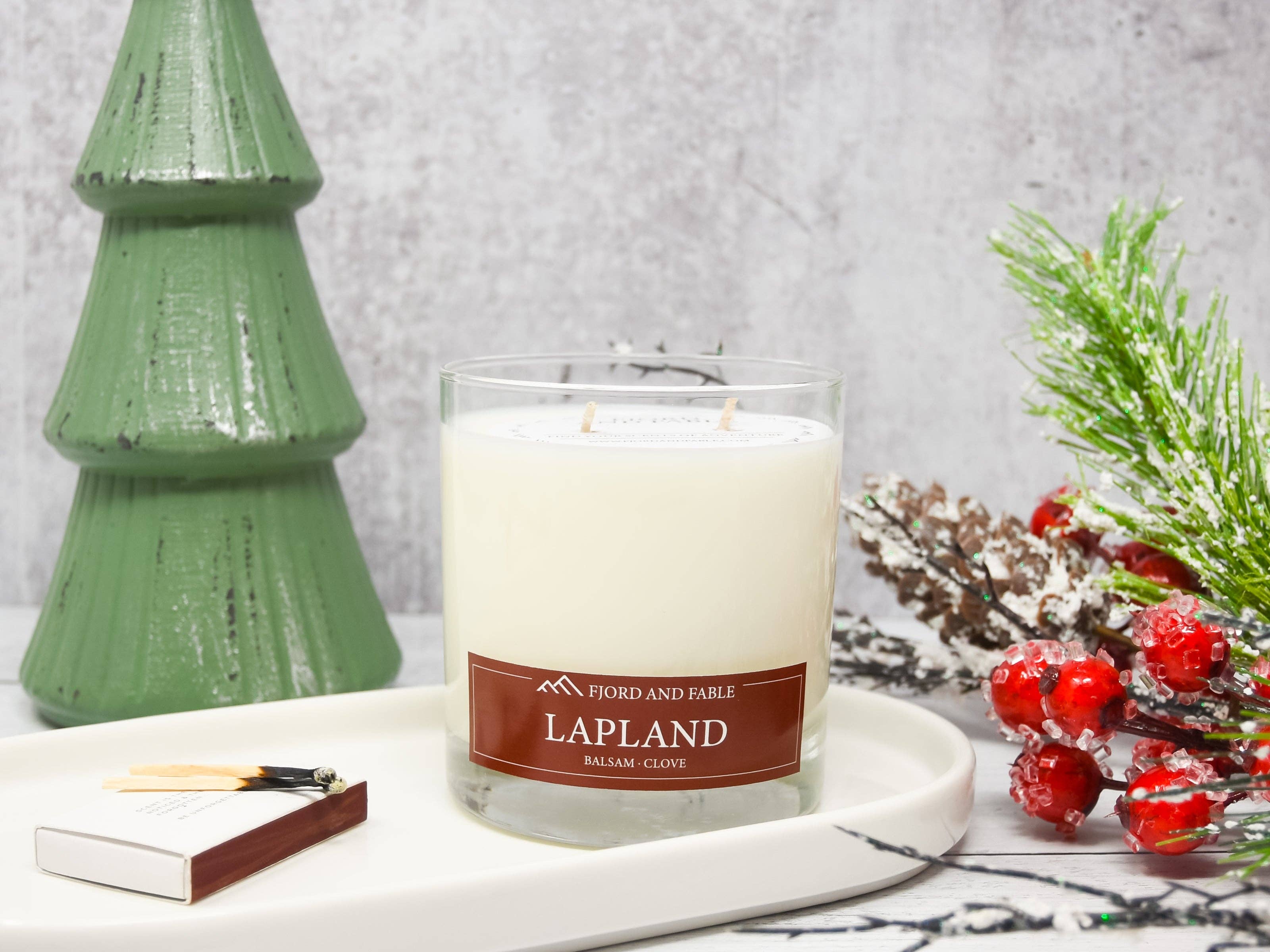 The Lapland Candle by Fjord & Fable features a balsam fir, clove, and cedar blend in an 8 oz glass with two wicks—perfect for creating a woodsy holiday atmosphere beside festive decor.