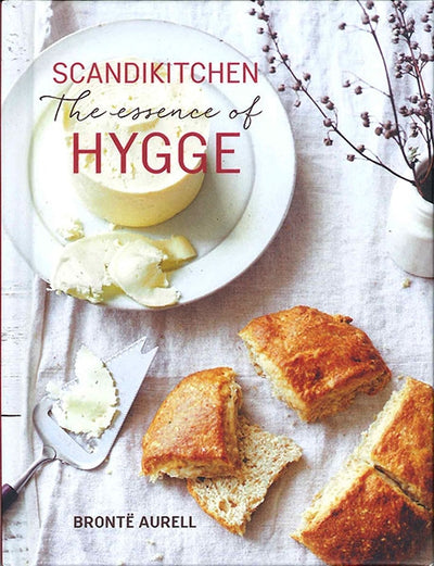 Cover of Book: ScandiKitchen: The Essence of Hygge by Bronte Aurell, showing bread, butter, a butter knife, and dried flowers on a white table—capturing the cozy warmth and comfort at the heart of hygge.
