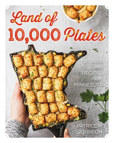 Cover of the book *Land of 10,000 Plates: Stories and Recipes from Minnesota* by Patrice M. Johnson, showcasing a tater tot hotdish arranged in a dish shaped like Minnesota. Parsley garnish and wild rice accompany it, enhancing beloved food traditions.