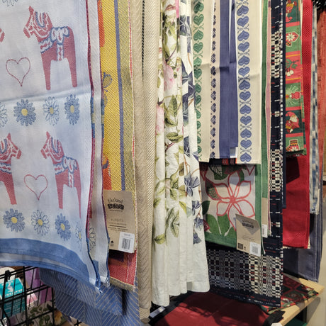 A display of various patterned textiles, including designs with hearts, floral prints, and geometric patterns, hanging vertically.
