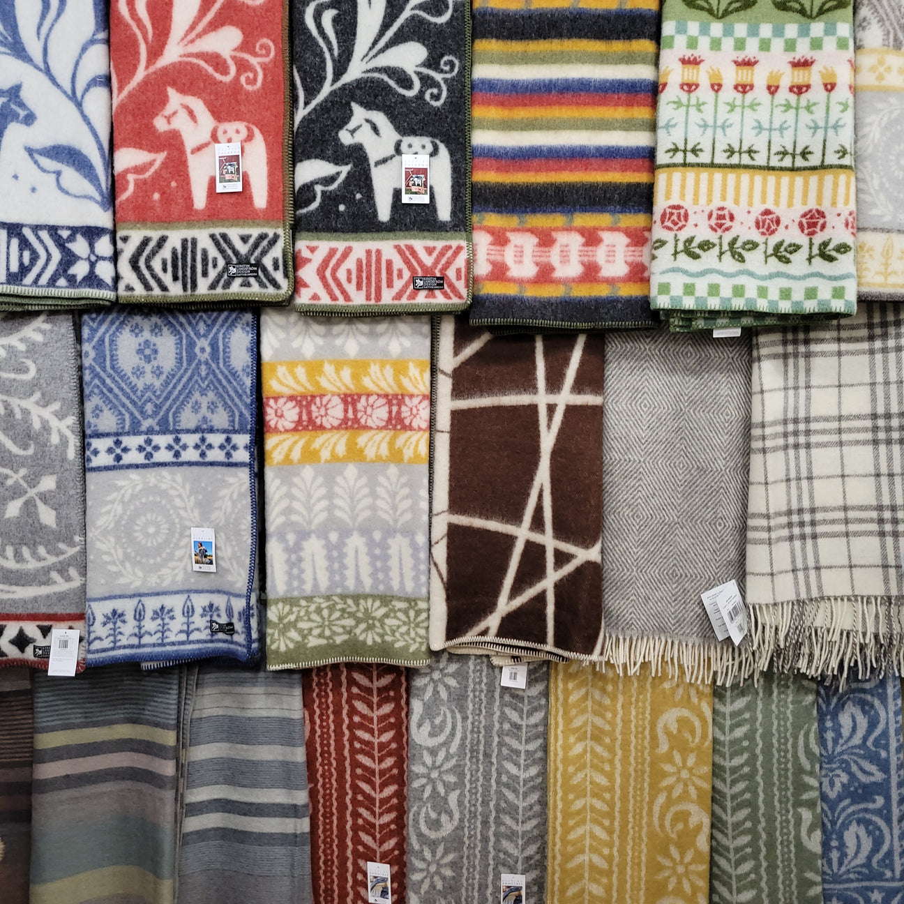 A display of colorful patterned blankets and shawls, featuring various designs including floral, geometric, and stripes, hung on a wall.