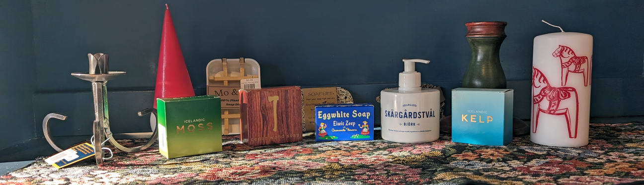A collection of soaps, liquid soap, candles, and a lotion bottle are displayed on a floral-patterned surface against a dark wall.