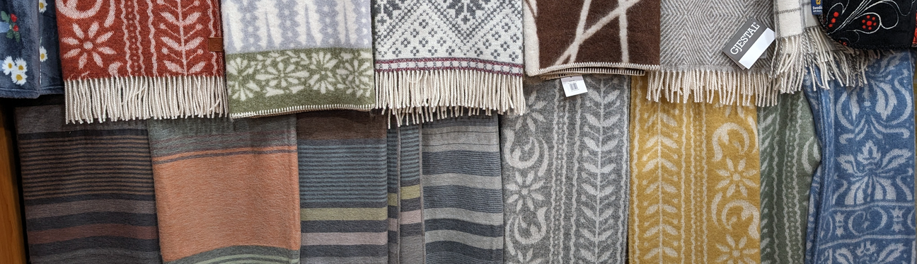 A variety of patterned and colorful woven textiles hang on a rack, each featuring different designs and fringed edges.
