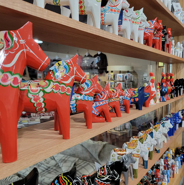 Rows of colorful Dala horse figurines are displayed on wooden shelves.