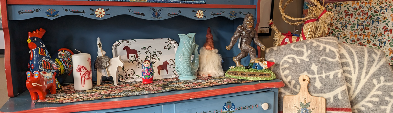 A blue shelf with colorful Scandinavian decor, including a rooster, candles, a wooden horse, vases, a gnome, and figurines. A patterned fabric and cutting board are also visible.